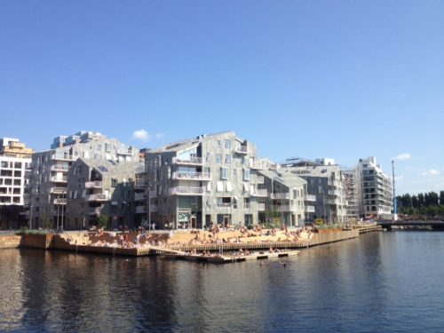 Bildet viser nye boligblokk hus i Bispevika i Oslo med Oslo Fjorden i forgrunnen en sommerdag når folk bader og visualiserer at om du har smågjeld og trenger å refinansiere det kan du bake det inn i boligen din.